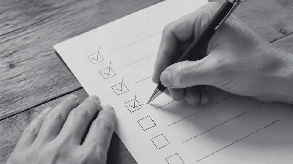 Main cochant les cases d'une checklist papier sur un bureau, illustrant la préparation des pièces pour domicilier une auto-entreprise